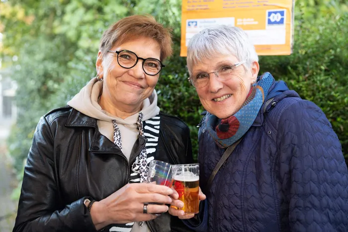 Zwei lächelnde Frauen halten Gläser mit Getränken hoch.