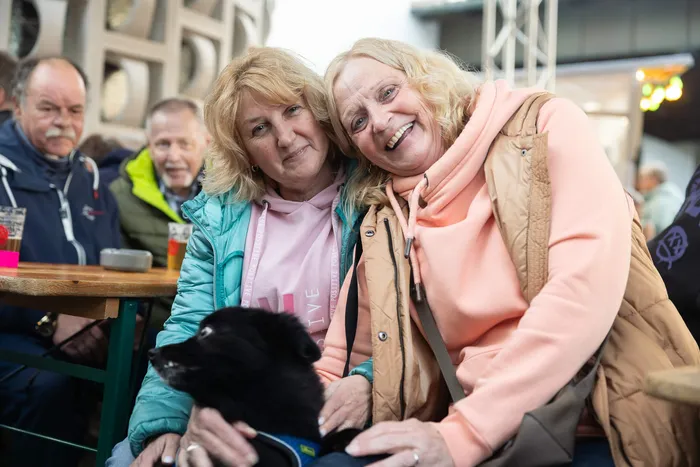 Zwei lächelnde Frauen halten einen kleinen schwarzen Hund im Arm bei einem Gemeindefest.
