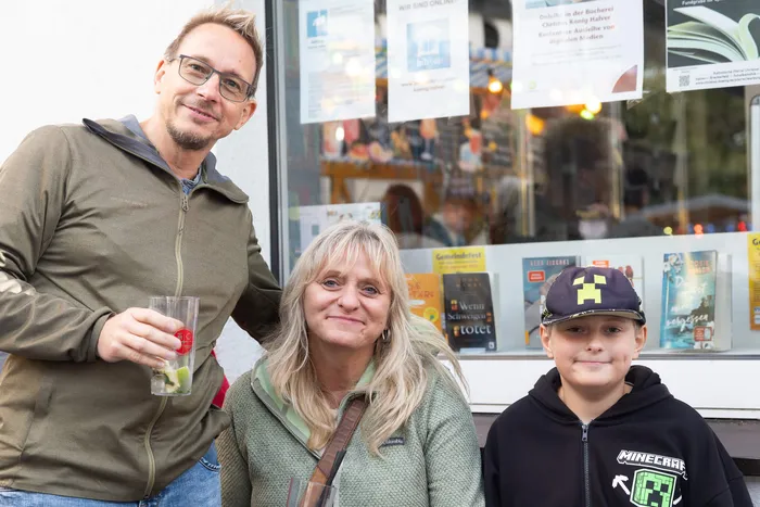 Ein Mann, eine Frau und ein Junge lächeln vor einem Schaufenster bei einem Gemeindefest in Halver.