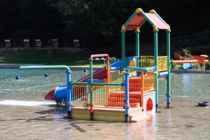 Bunter Wasserspielplatz mit Rutschen in einem flachen Becken des Waldfreibads Herpine.