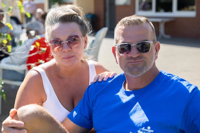 Eine Frau in einem weißen Top und ein Mann in einem blauen T-Shirt mit Sonnenbrillen blicken in die Kamera.