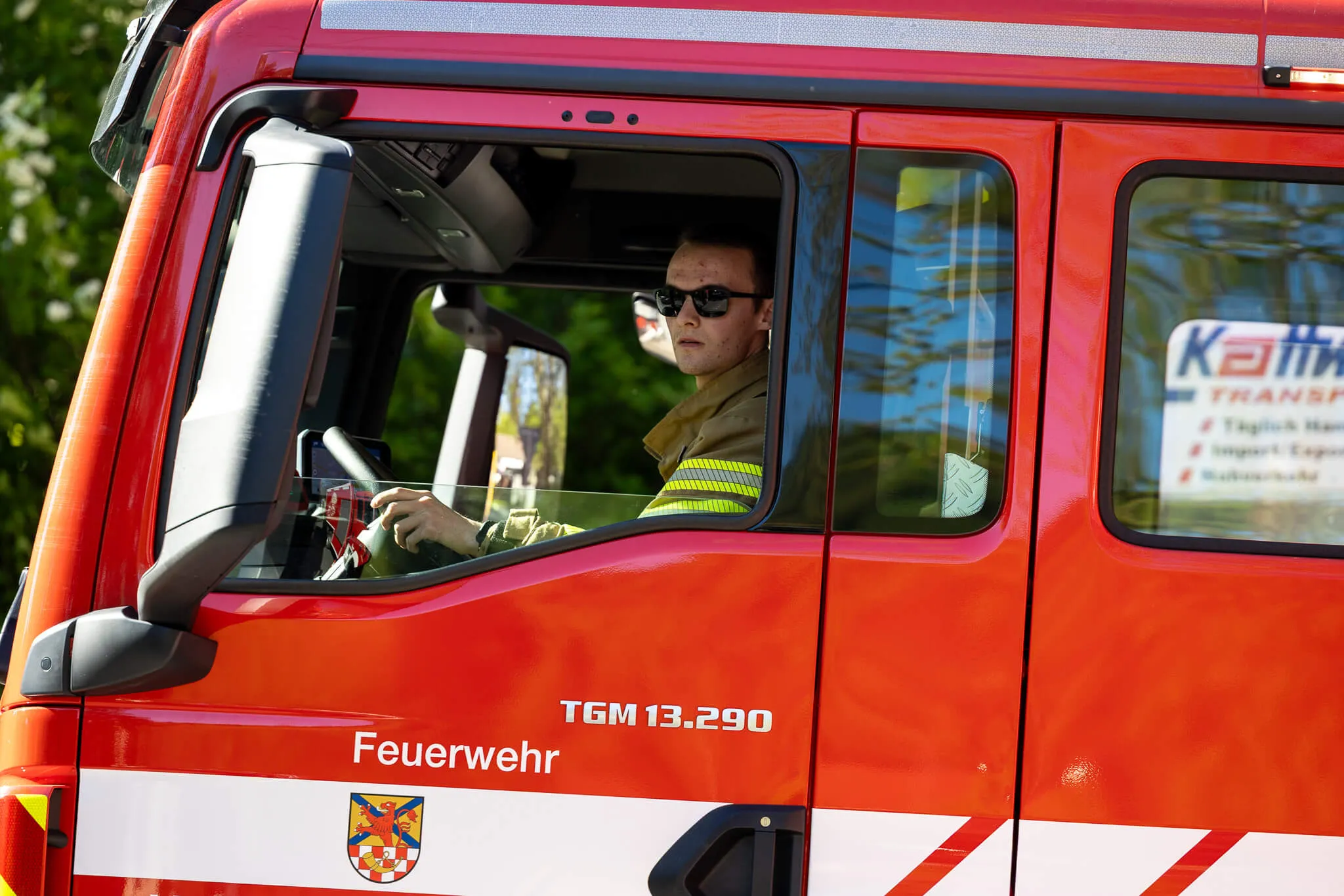 Feuerwehrmann am Steuer eines roten Löschfahrzeugs mit der Aufschrift „Feuerwehr“ und dem Wappen der Gemeinde Oberbrügge.