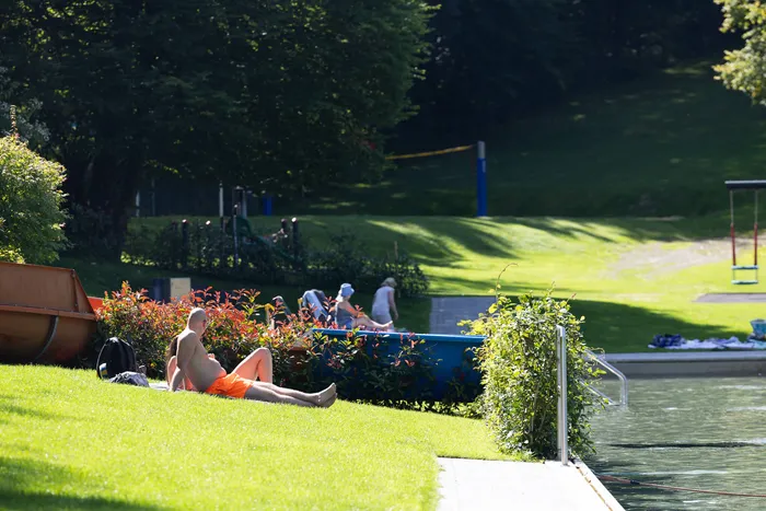 Ein Mann in orangefarbener Badehose sonnt sich auf einer Rasenfläche am Rand eines Schwimmbeckens im Waldfreibad Herpine.