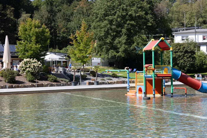 Ein buntes Wasserspielgerät mit einer roten Rutsche steht in einem flachen Schwimmbecken im Waldfreibad Herpine.