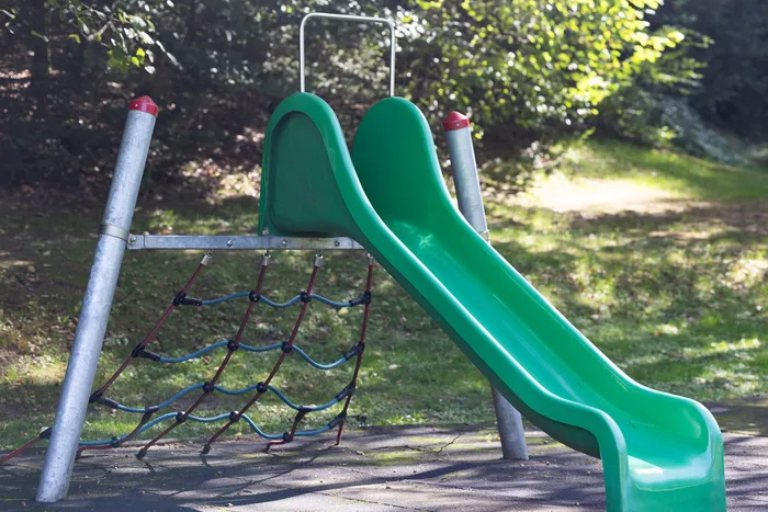 Eine grüne Rutsche und ein Kletternetz an einem Spielgerät im Waldfreibad Herpine.