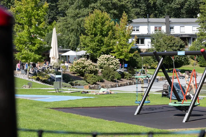 Spielplatz mit Schaukeln vor einer Liegewiese und Bäumen im Waldfreibad Herpine.