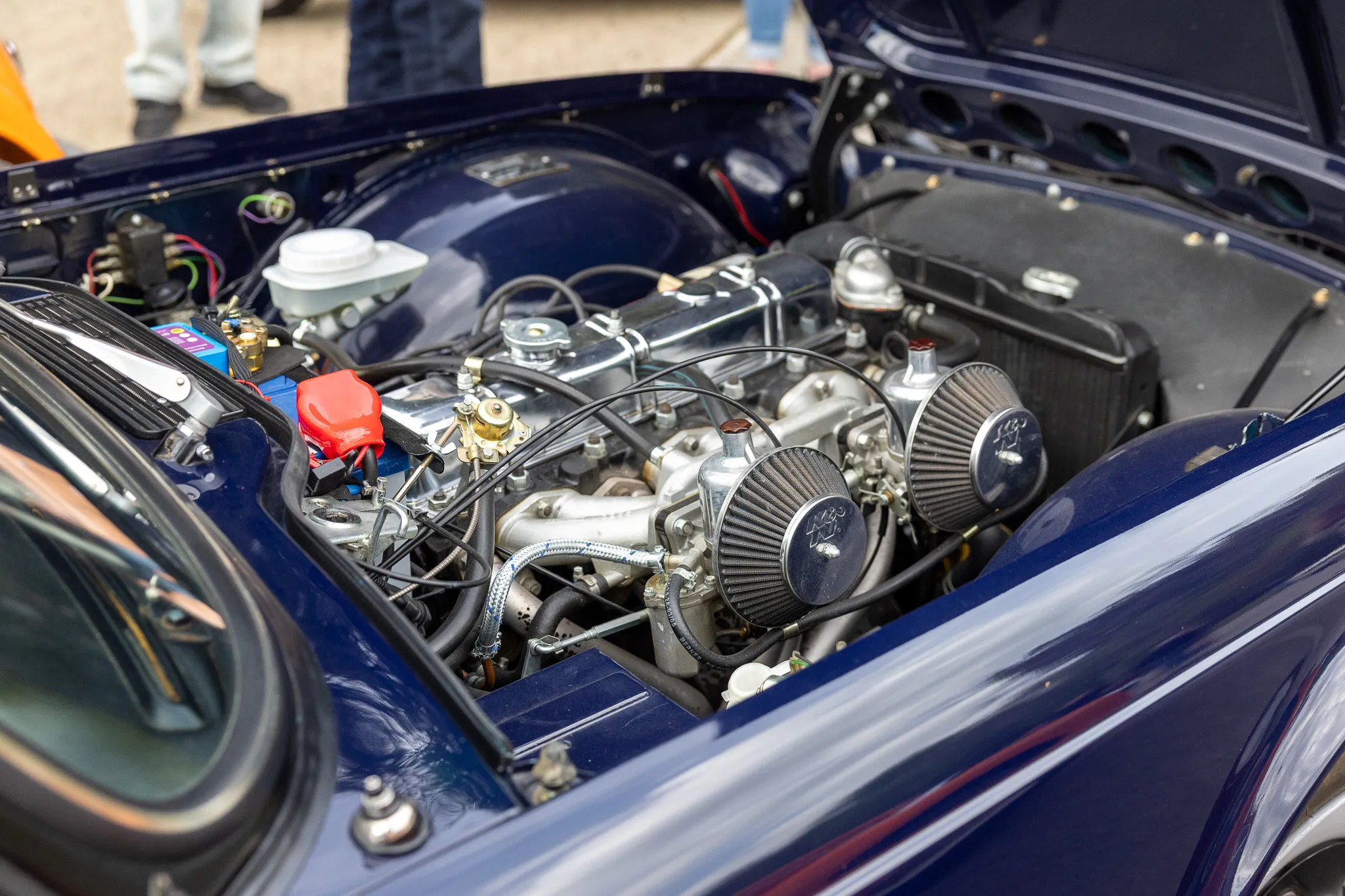 Detailaufnahme des geöffneten Motorraums eines dunkelblauen Oldtimers mit mehreren Zylindern und Luftfiltern.