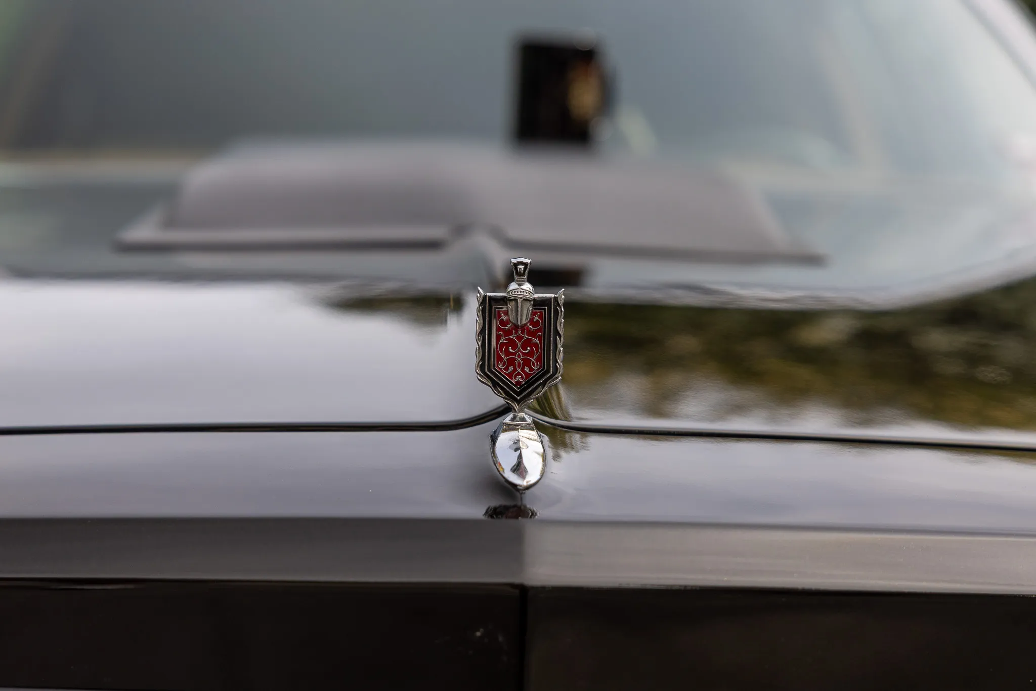 Chromglänzendes Kühleremblem in Form eines Wappens auf der Motorhaube eines Oldtimers.