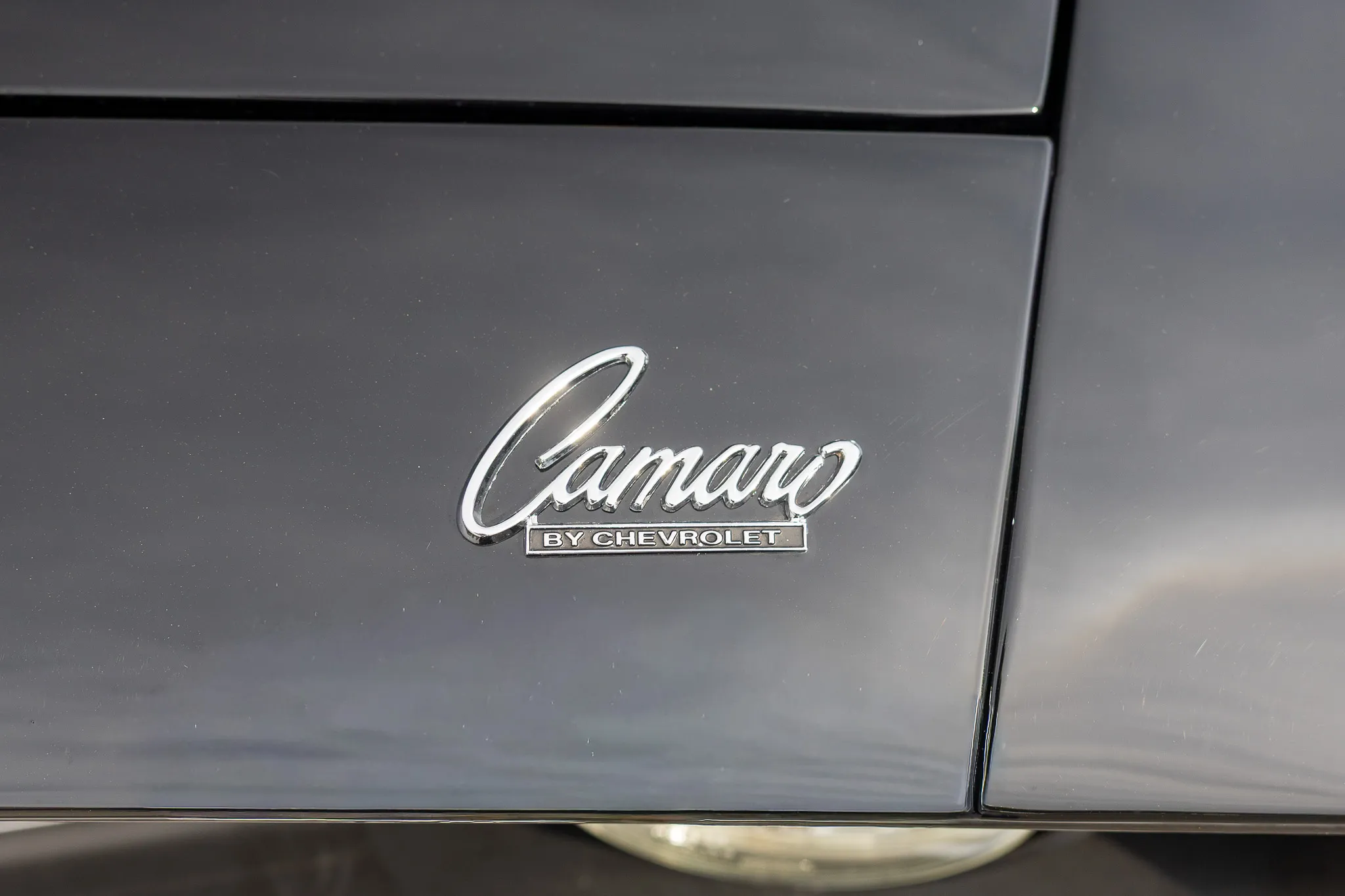 Chrom-Emblem „Camaro by Chevrolet“ auf der dunklen Karosserie eines Oldtimers.