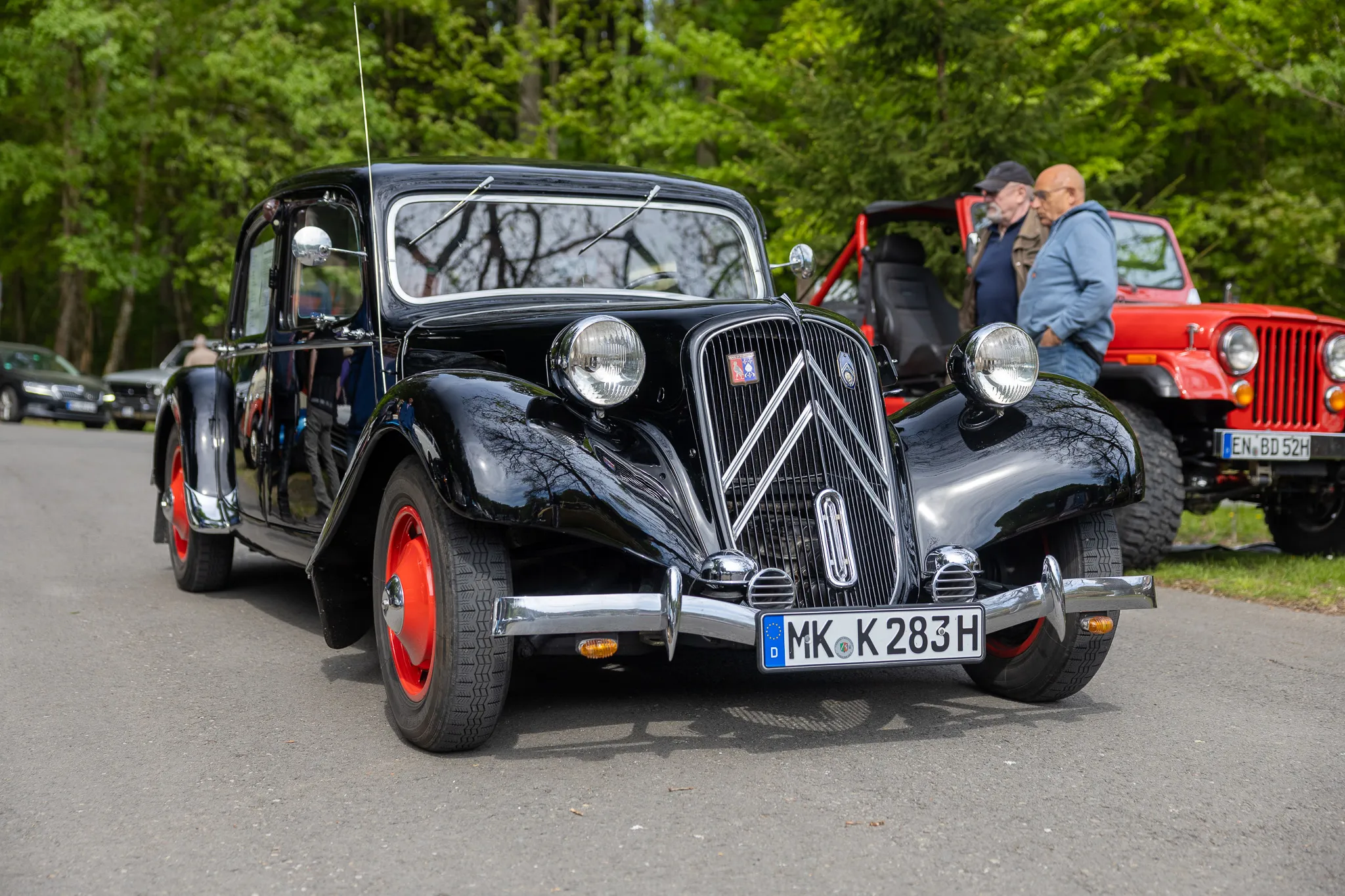 Schwarzer Citroën Traction Avant steht auf einer Wiese, umgeben von weiteren Oldtimern und Besuchern eines Oldtimertreffens.