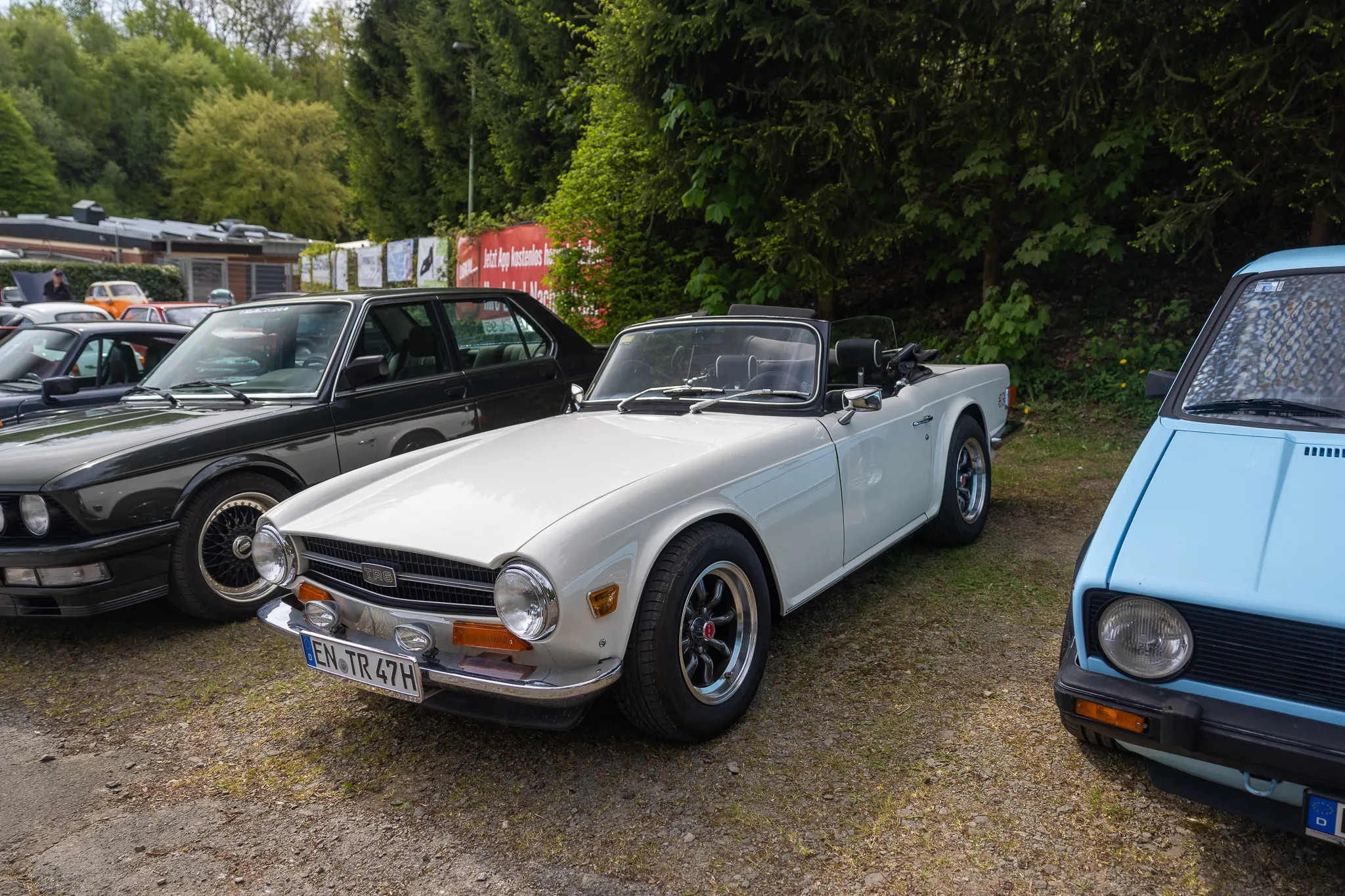 Weißer Triumph Spitfire steht auf einem Oldtimertreffen neben anderen Fahrzeugen.
