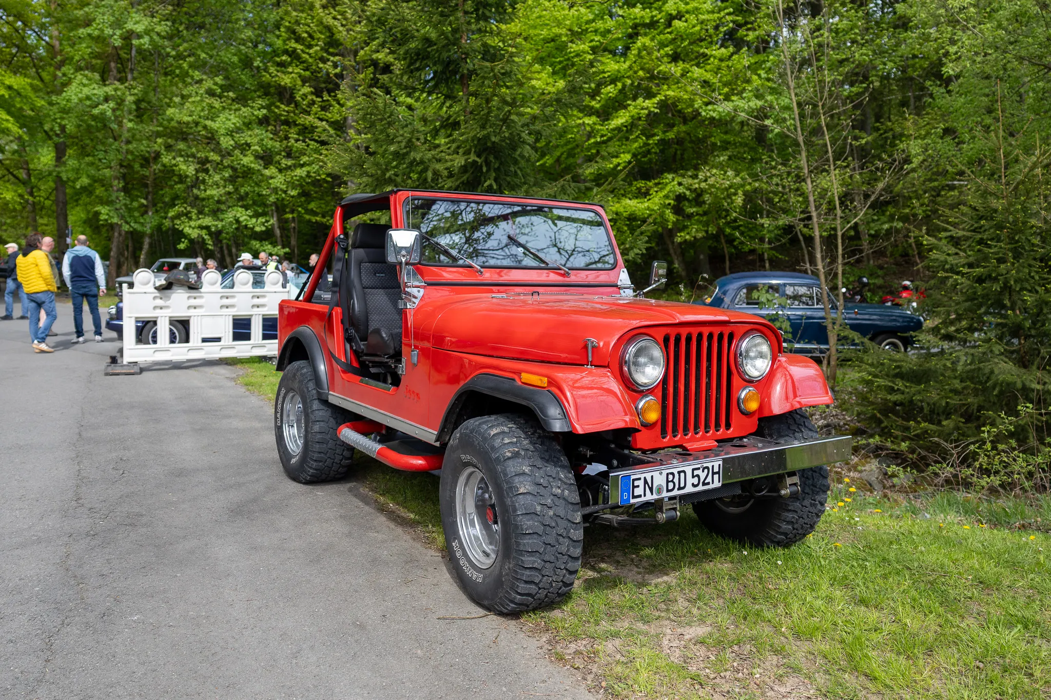 Roter Jeep CJ-7 steht auf einem Parkplatz vor Bäumen, Kennzeichen EN-BD 52H.