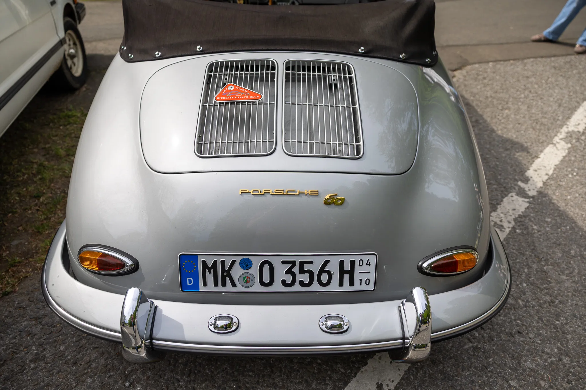 Heckansicht eines silbergrauen Porsche 356 mit Kennzeichen, der auf einem Oldtimertreffen steht.