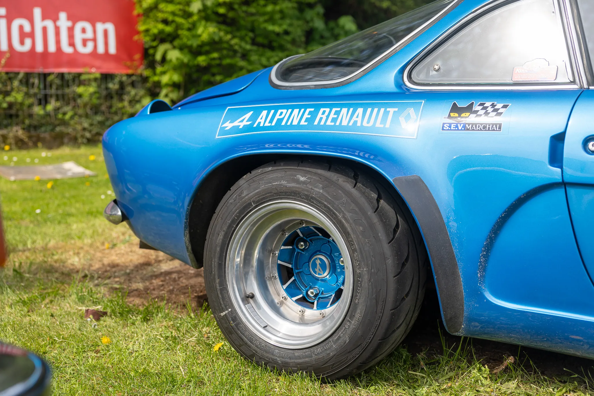 Blauer Alpine Renault Sportwagen mit Rennstreifen und silbernen Felgen steht auf einer Wiese.