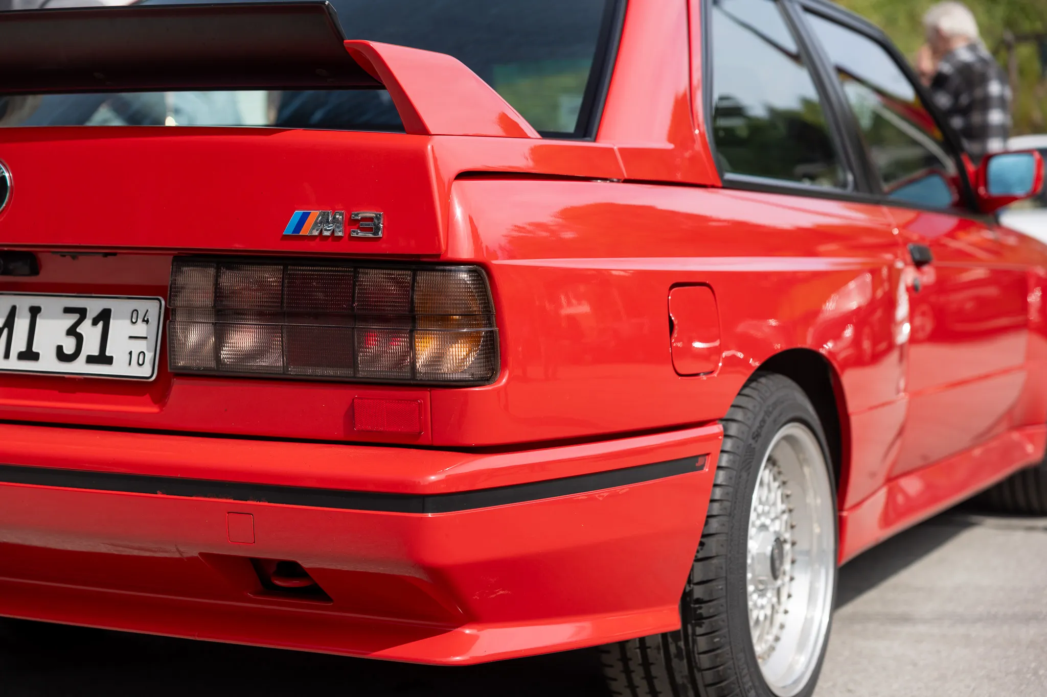 Rotes Heck eines klassischen BMW M3 mit Kennzeichen, Detailaufnahme des Rücklichts und des Spoilers.