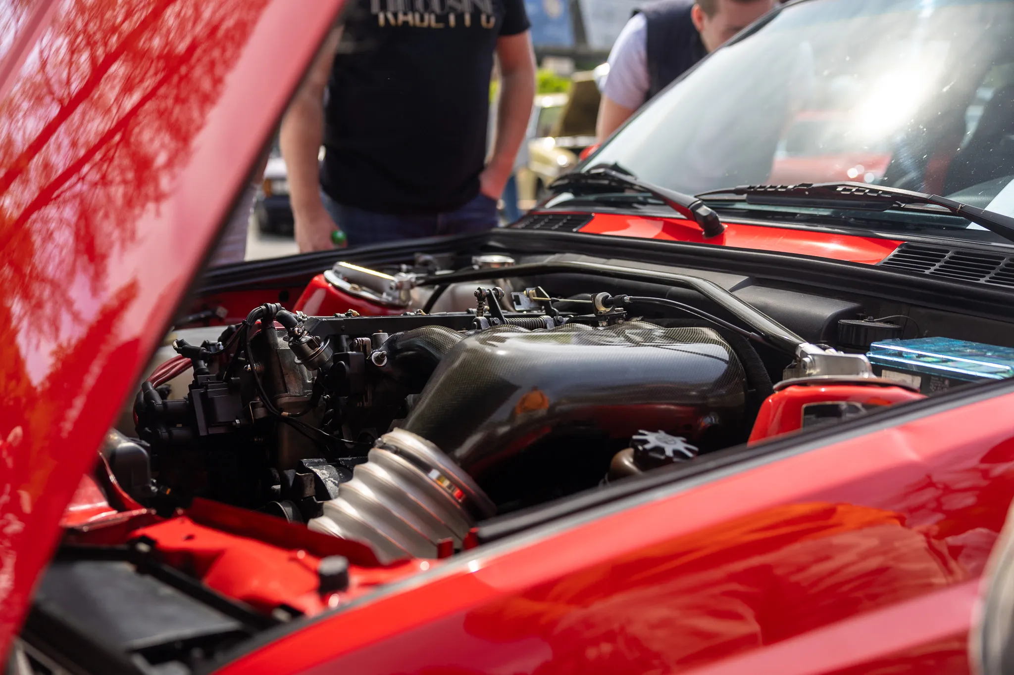 Detailaufnahme des geöffneten Motorraums eines roten Oldtimers mit komplexer Technik und Carbon-Elementen.
