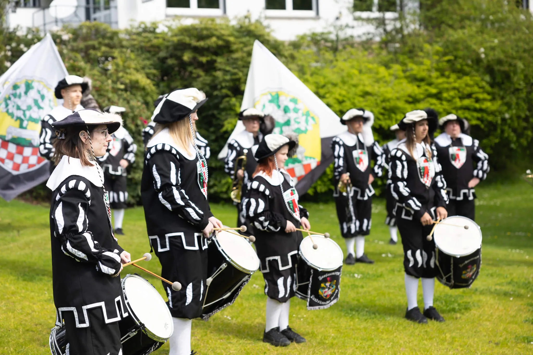 Trommler in historischen Kostümen mit weißen Handschuhen und Dreispitzen spielen auf einer grünen Wiese vor Zuschauern.