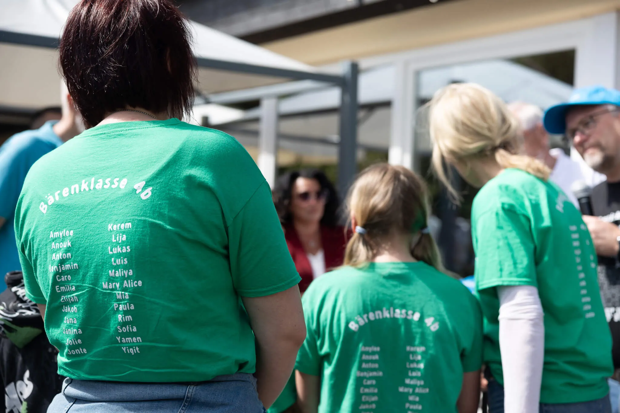 Mehrere Personen mit grünen T-Shirts mit den Namen der Bärenklasse 4b auf dem Rücken stehen im Freien zusammen.
