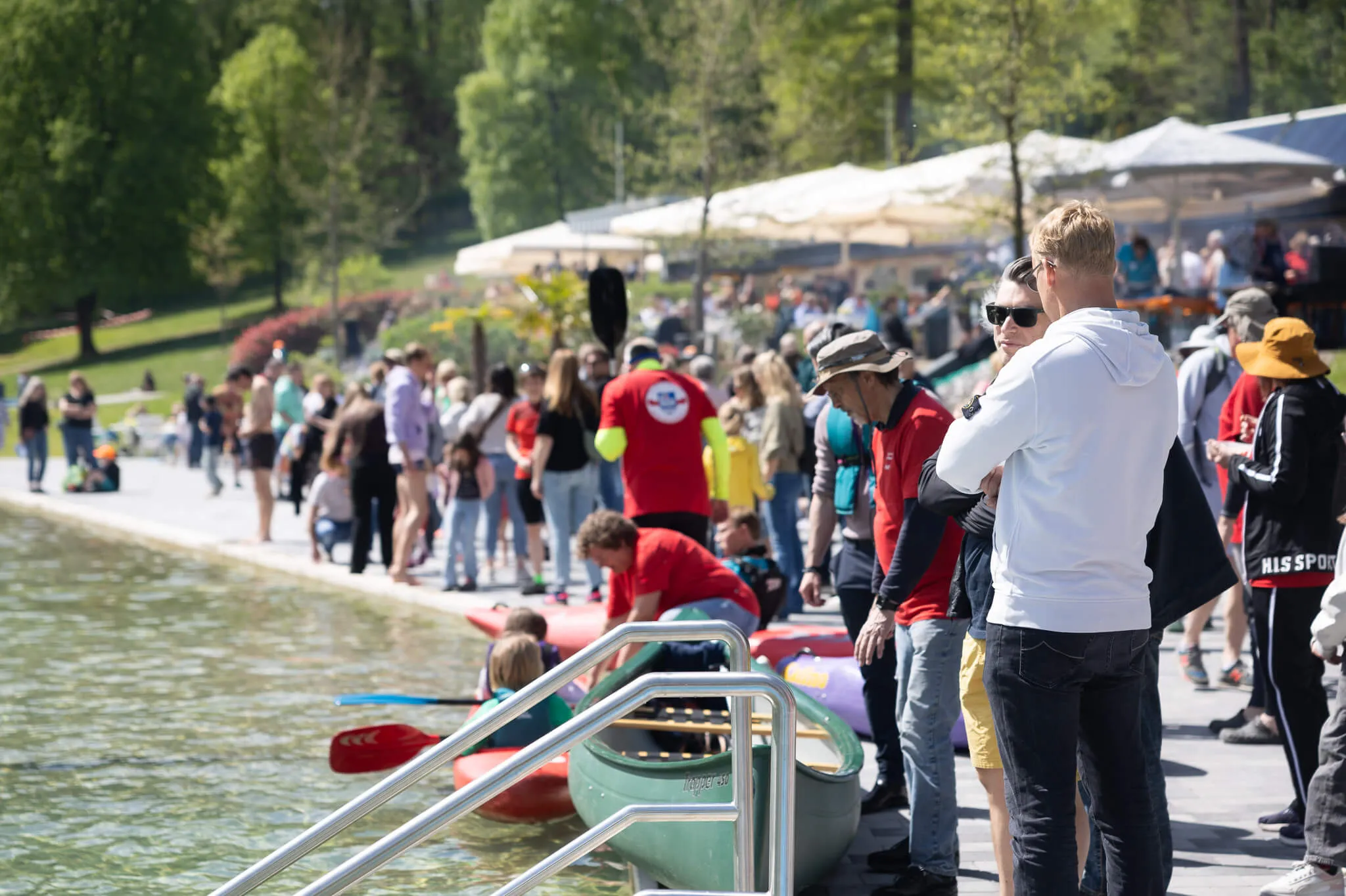 Menschen beobachten vom Ufer aus die Boote auf dem See während der Saisoneröffnung der Herpine in Halver.