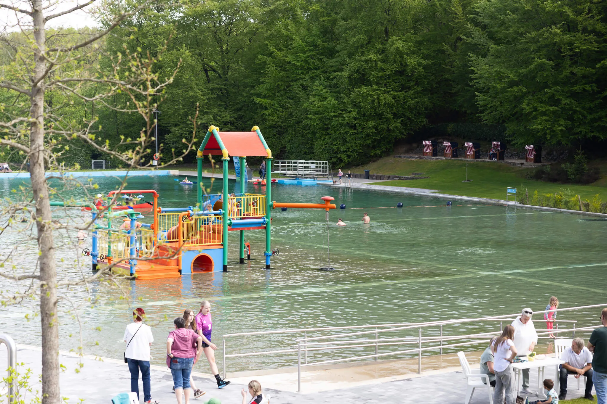 Blick auf das Freibad Herpine in Halver mit bunten Wasserspielgeräten und Badegästen im Wasser und am Ufer.