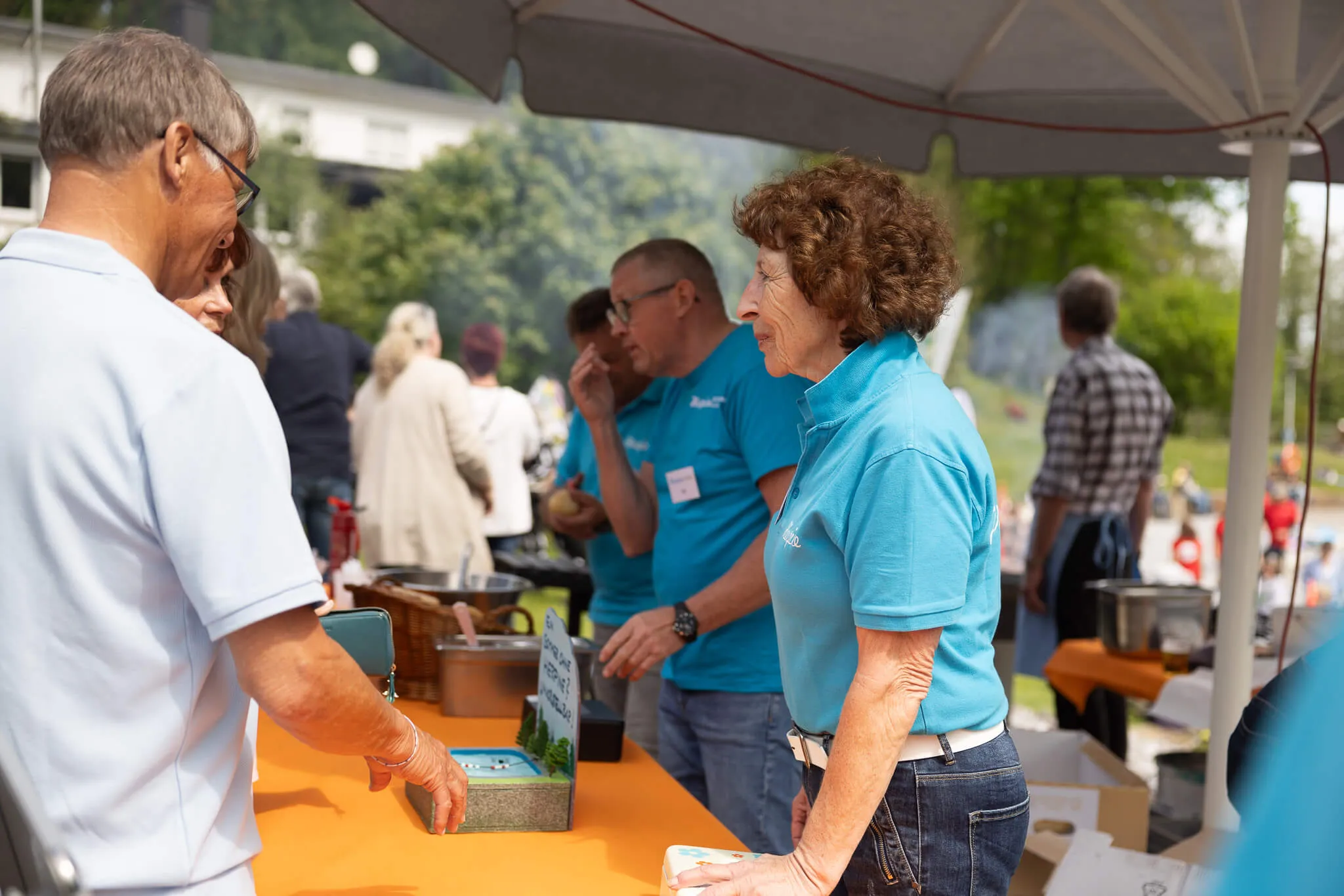 Zwei Personen stehen an einem Infostand auf der Saisoneröffnung der Herpine in Halver, im Hintergrund weitere Besucher und ein Grillstand.