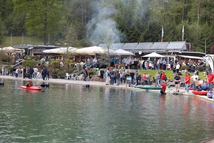 Blick auf die belebte Herpine in Halver zur Saisoneröffnung mit Besuchern an Tischen unter Sonnenschirmen und Booten auf dem See.