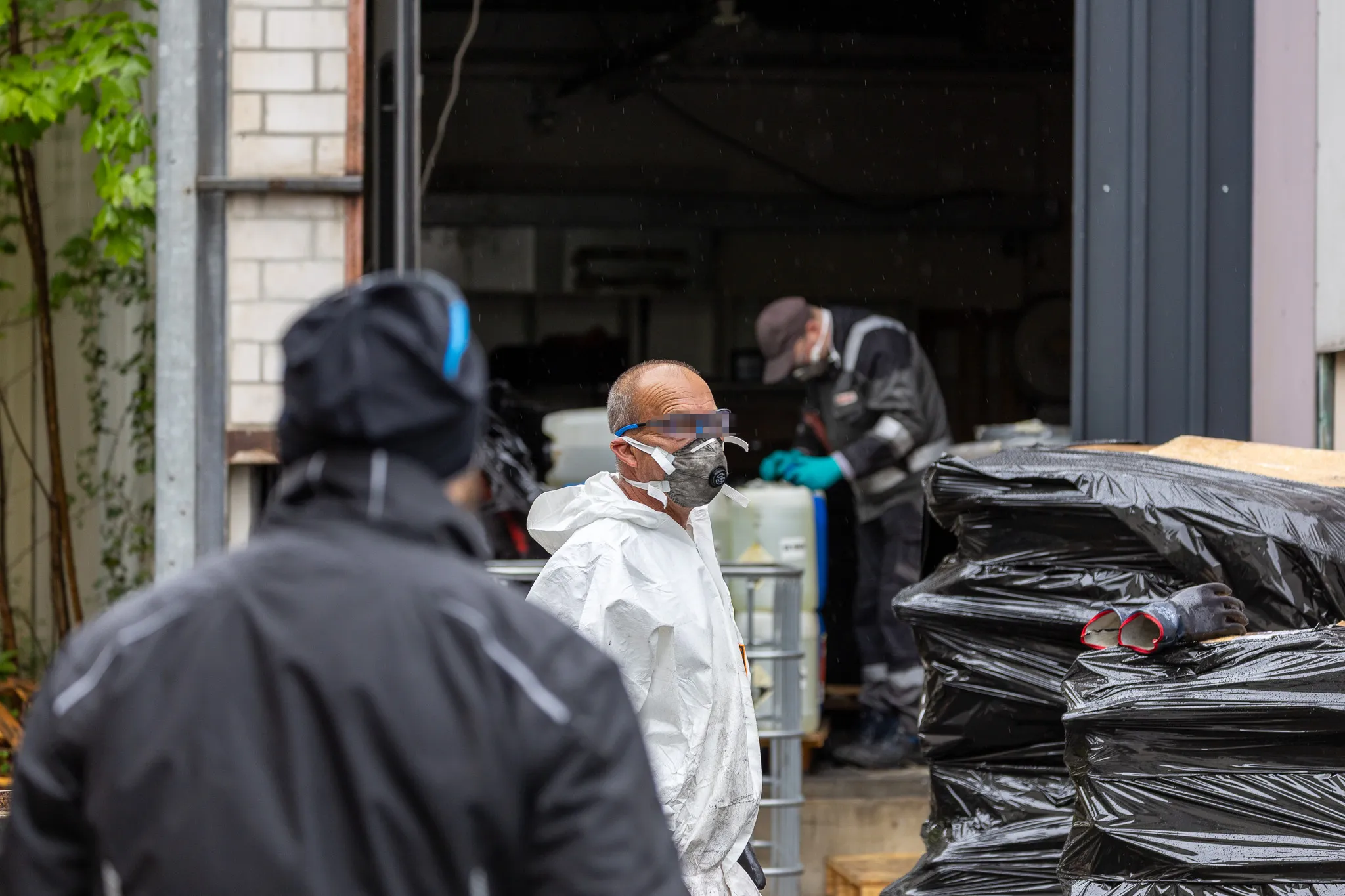Personen in Schutzanzügen und Masken räumen einen Raum aus, möglicherweise im Zusammenhang mit einem Drogenlabor.