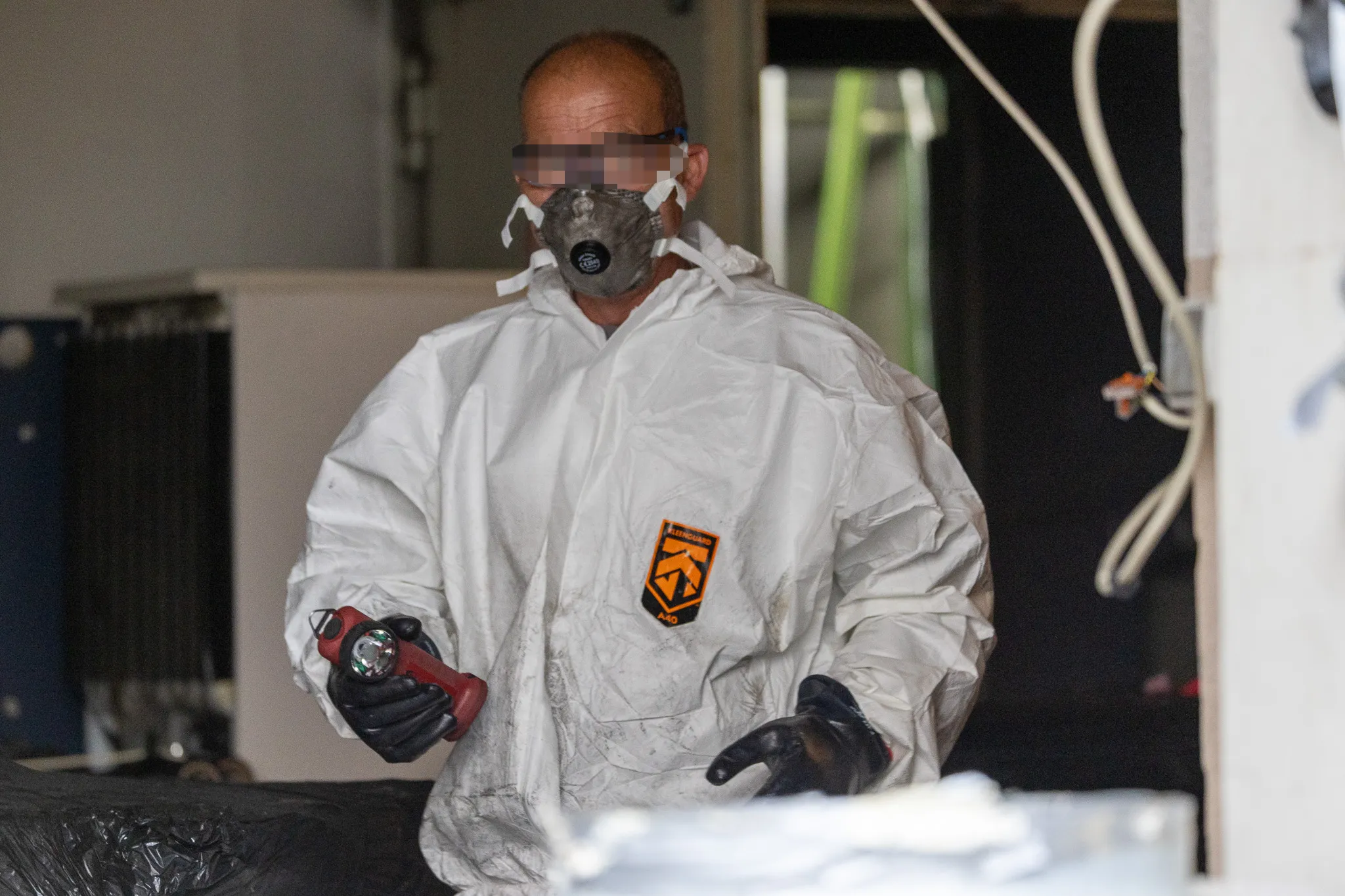 Person in Schutzanzug und Maske hält eine Sprühflasche, während sie ein Labor räumt.
