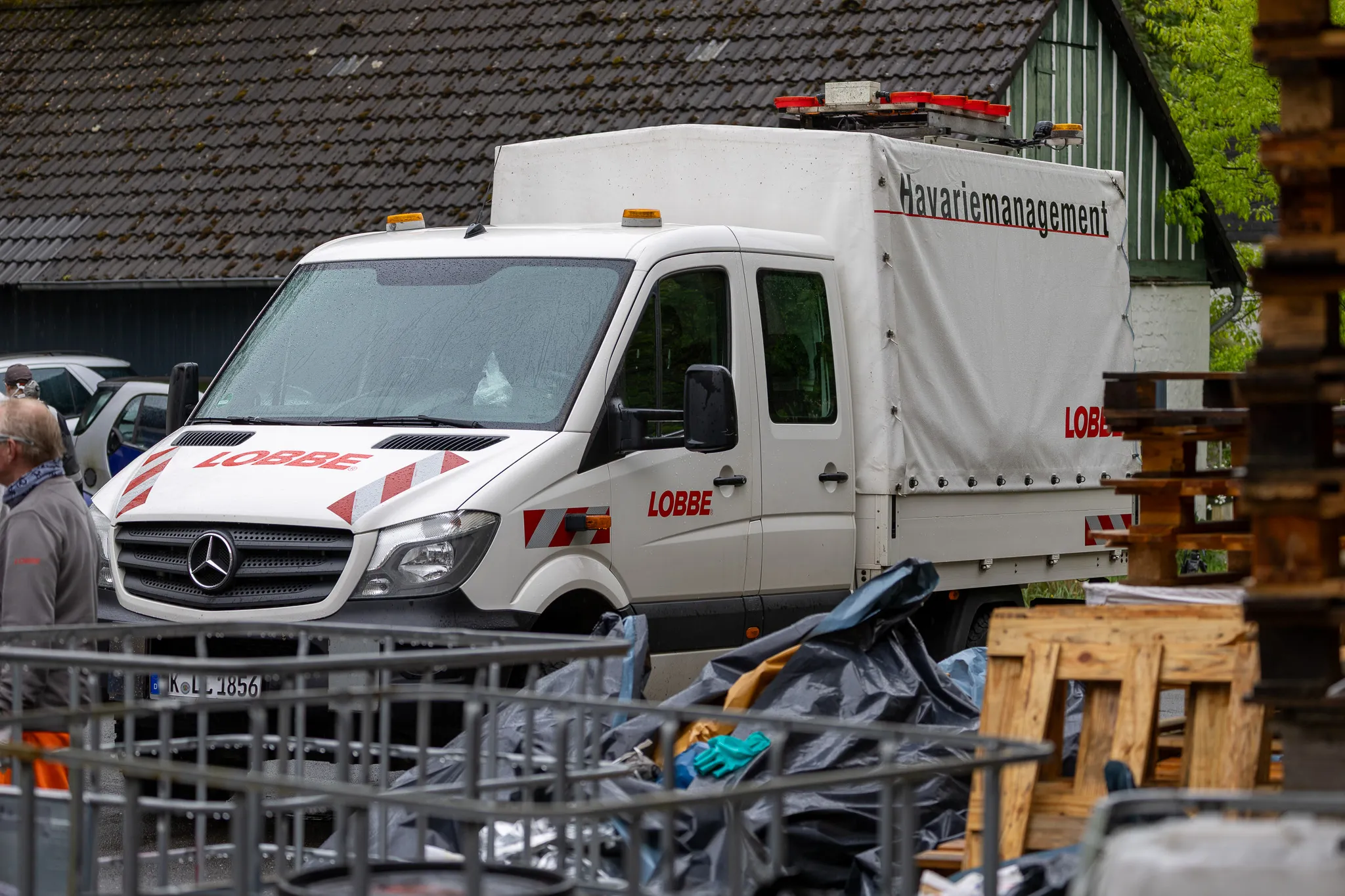 Weißer Transporter des Entsorgungsdienstleisters Lobbe mit Aufschrift „Havariemanagement“ steht vor einem Gebäude, im Vordergrund Metallgitter und Paletten.