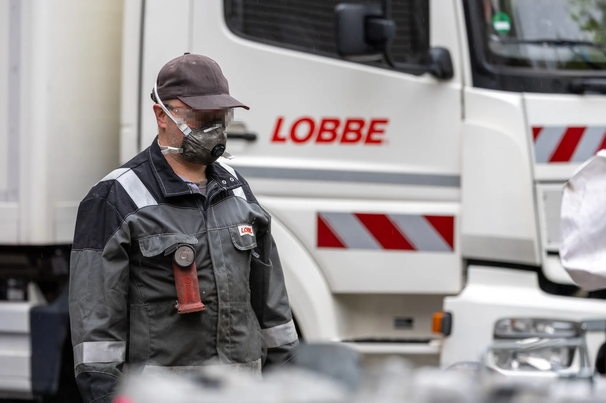 Ein Mitarbeiter des Entsorgungsdienstleisters Lobbe mit Schutzmaske und Overall steht vor einem weißen LKW des Unternehmens.