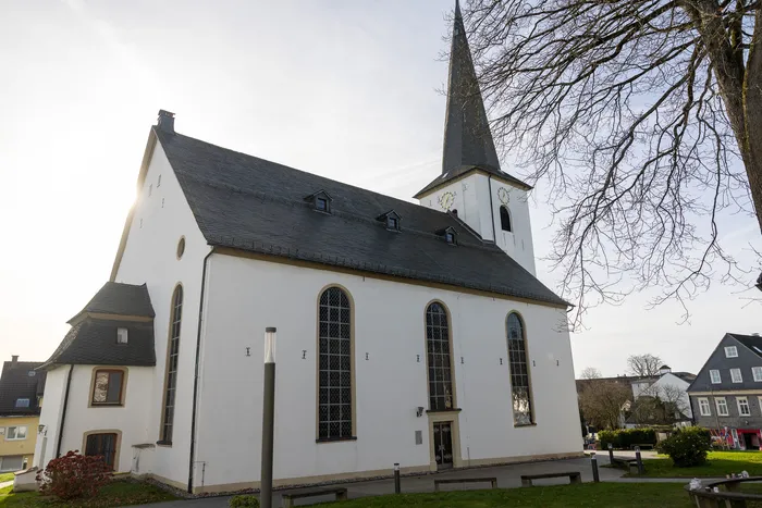 Die weiße Nicolai Kirche in Halver mit ihrem hohen, spitzen Kirchturm und mehreren spitzbogigen Fenstern.