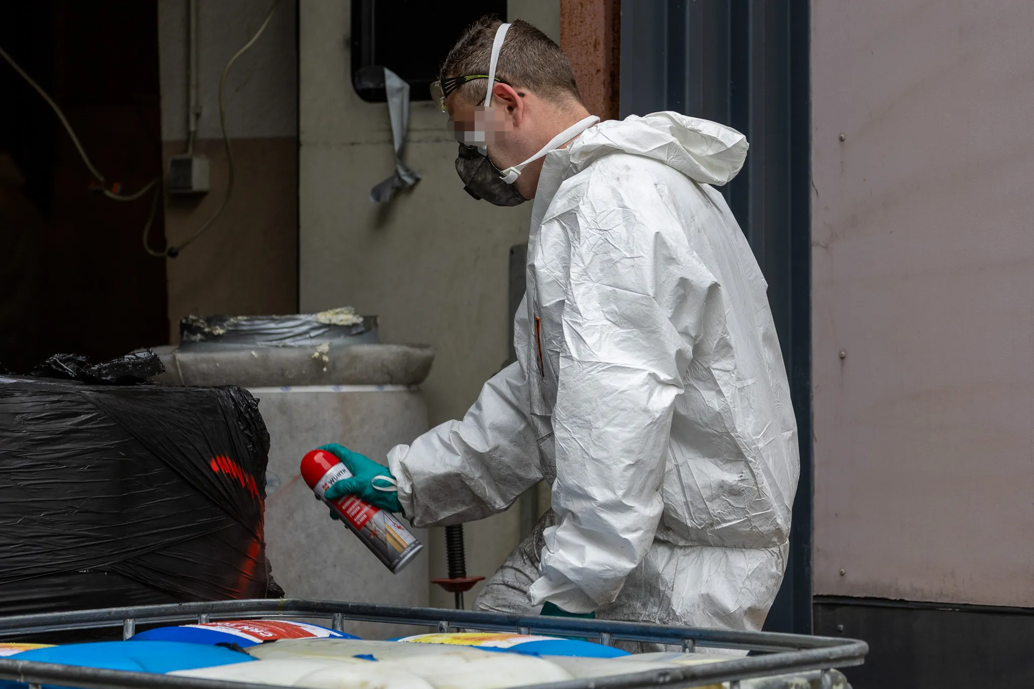 Person in Schutzanzug und Maske sprüht eine Dose auf eine schwarze Plane während der Räumung eines vermuteten Drogenlabors.