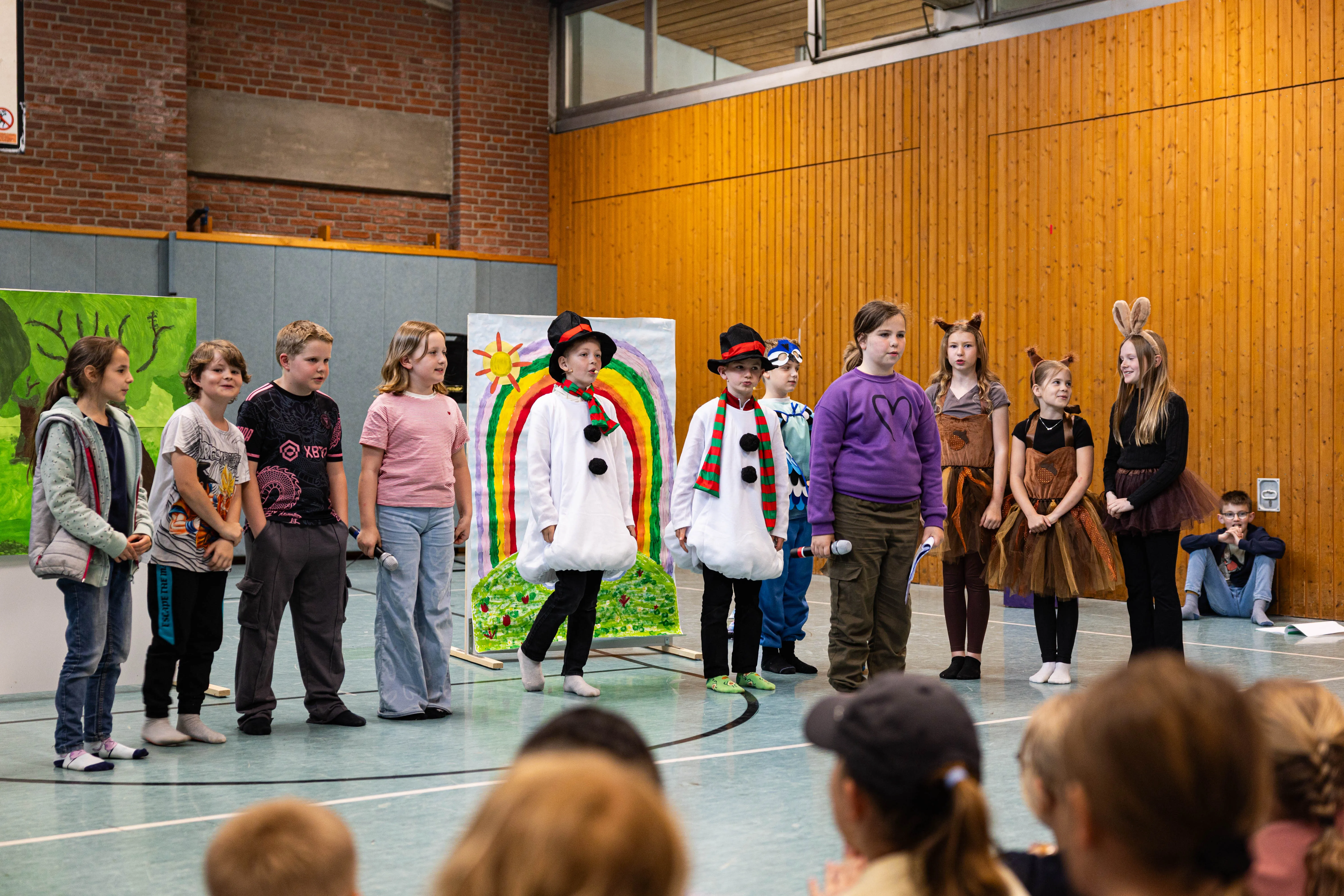 Schülerinnen und Schüler der Servatiusschule führen in Kostümen ein Theaterstück auf, im Hintergrund eine bunt bemalte Kulisse und Zuschauer.