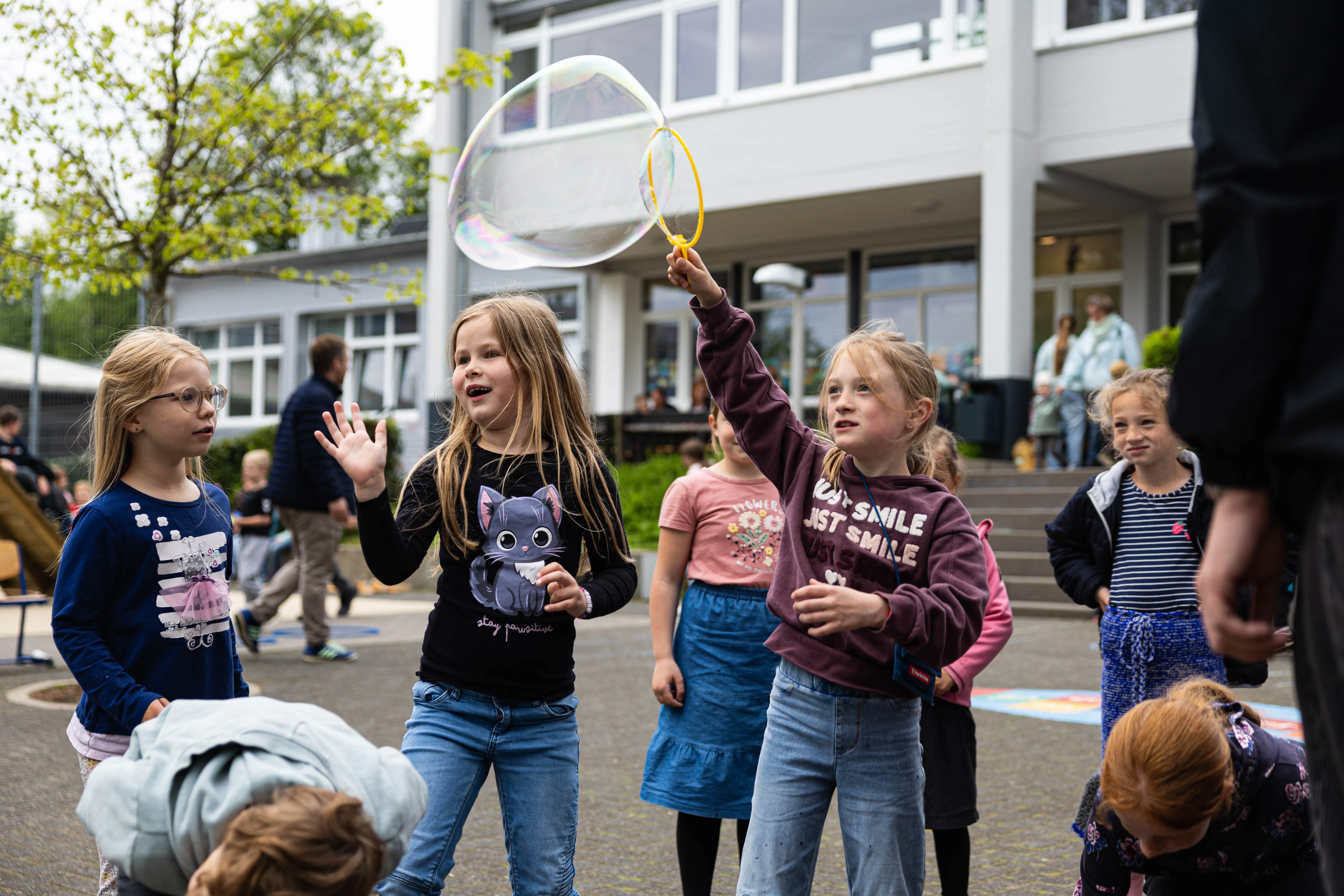 Kinder spielen Seifenblasen vor dem Gebäude der Servatiusschule während des Schulfests.