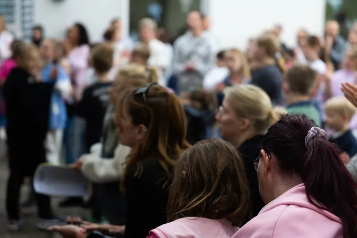 Eine Menschenmenge sitzt und steht vor einer Bühne, viele Kinder sind dabei. Im Vordergrund sind die Köpfe von Zuschauern zu sehen.
