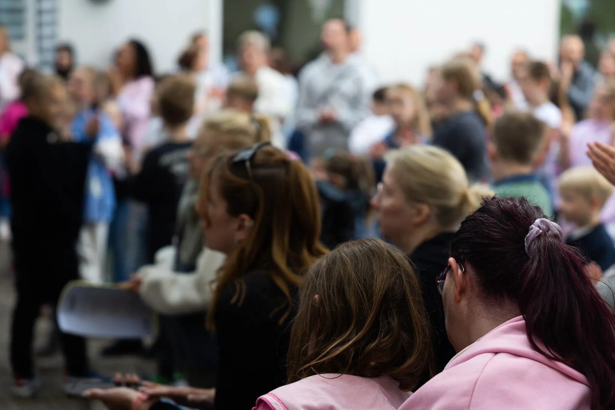 Eine Menschenmenge sitzt und steht vor einer Bühne, viele Kinder sind dabei. Im Vordergrund sind die Köpfe von Zuschauern zu sehen.
