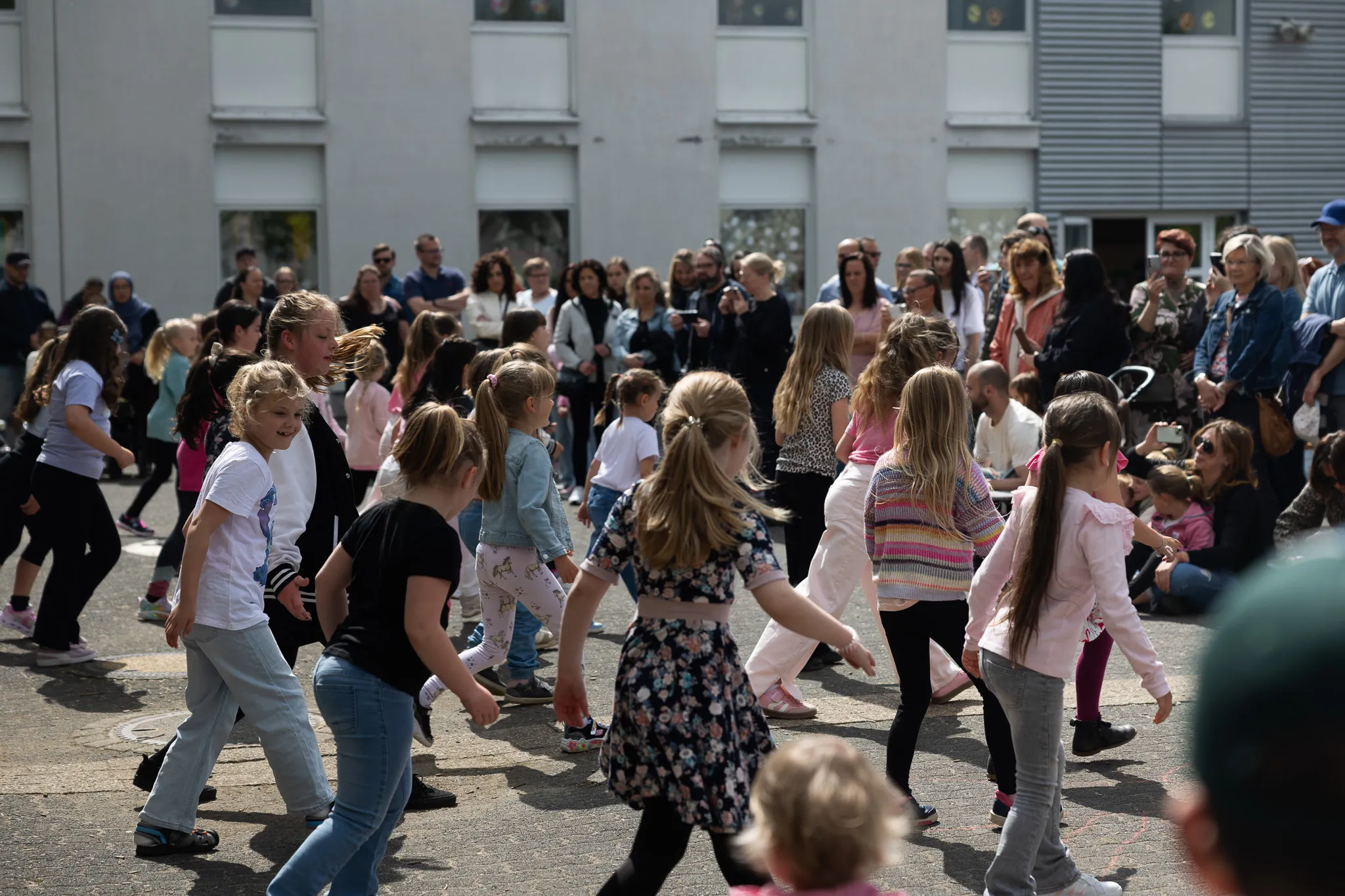 Eine Gruppe von Kindern tanzt im Freien vor einer Menschenmenge, die das Fest der Regenbogenschule beobachtet.