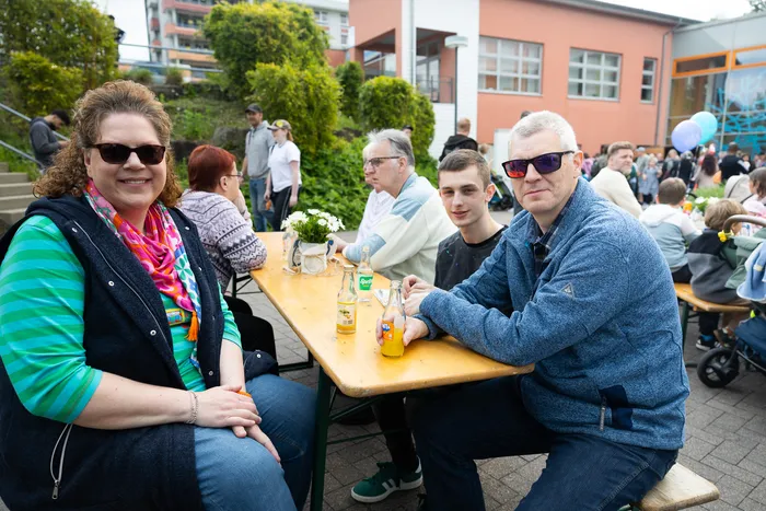 Zwei Frauen und zwei Männer sitzen an einem Biertisch vor einer Schule, trinken Bier und unterhalten sich während eines Jubiläumsfestes.