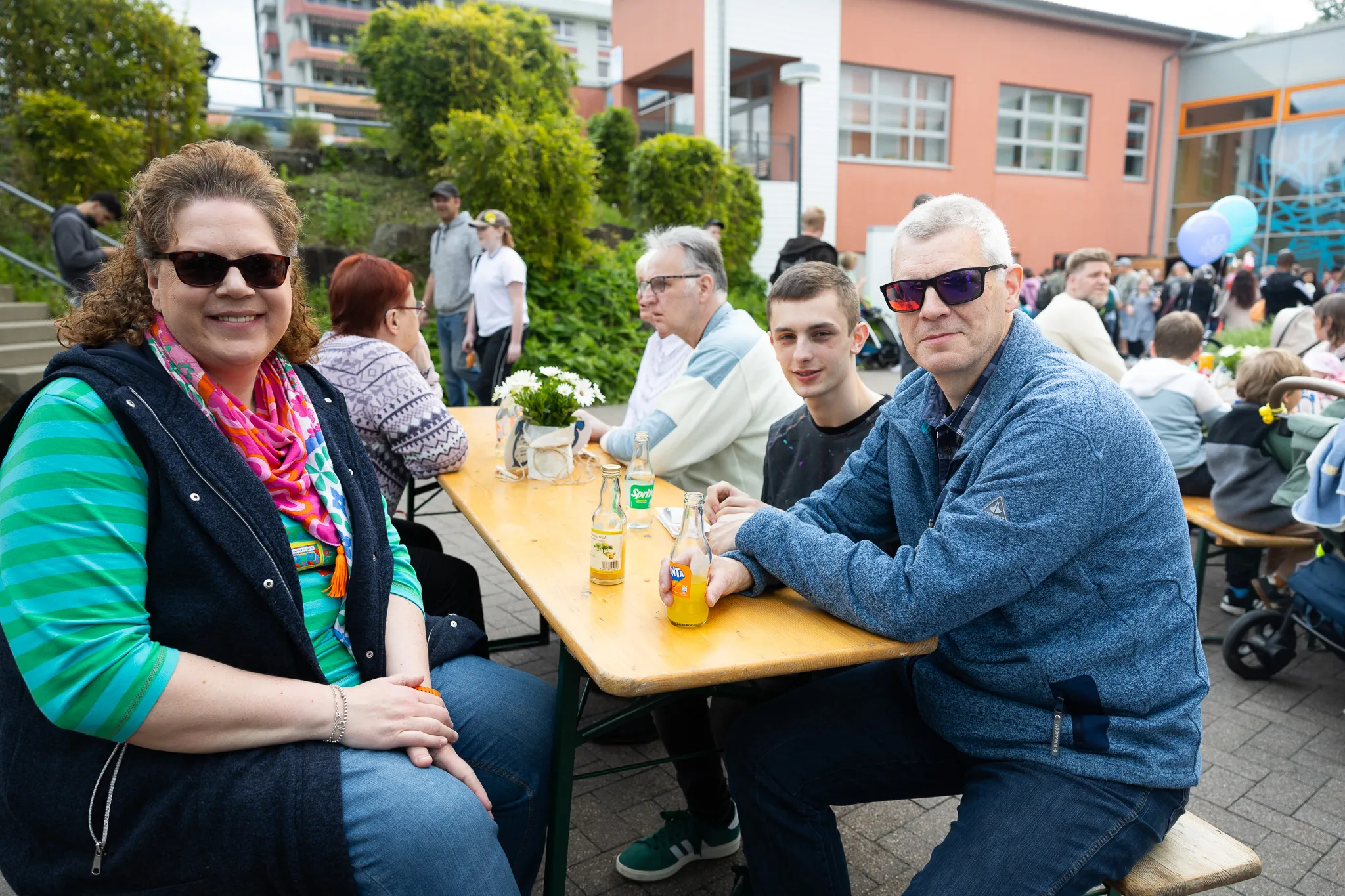 Zwei Frauen und zwei Männer sitzen an einem Biertisch vor einer Schule, trinken Bier und unterhalten sich während eines Jubiläumsfestes.