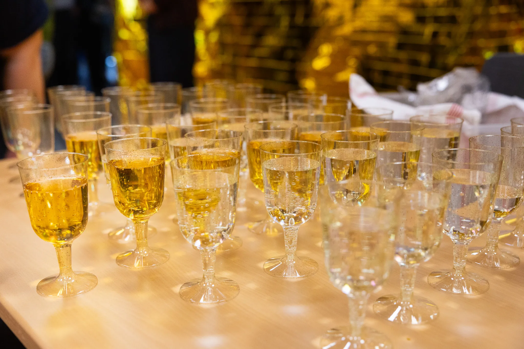 Reihe gefüllter Champagnergläser auf einem Holztisch, im Hintergrund goldene Folienvorhänge zur Feier des 50-jährigen Bestehens der Schule an der Höh.