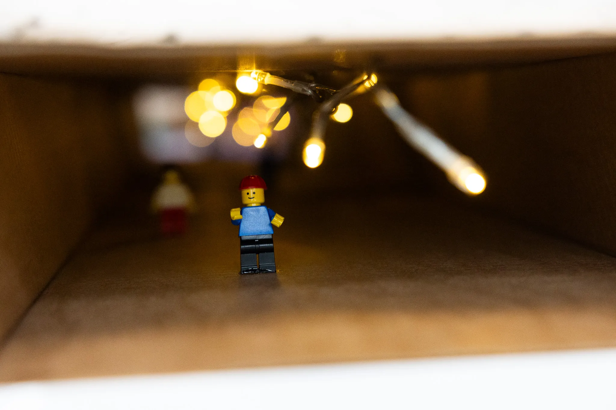 Eine Lego-Figur mit roter Mütze steht in einem dunklen Tunnel aus Pappe, im Hintergrund verschwommene Lichter.