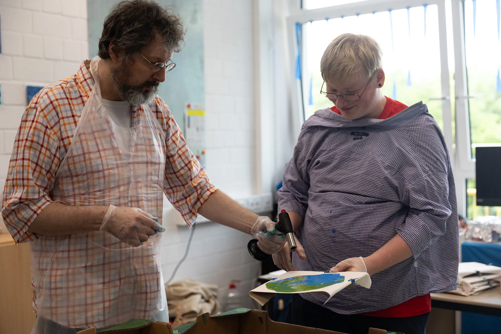 Zwei Personen arbeiten gemeinsam an einem farbigen Bild, möglicherweise im Rahmen eines Kunstprojekts zur Schulfeier.