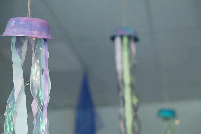 Selbstgebastelte Quallen aus Papier und Stoffbändern hängen als Dekoration von der Decke.