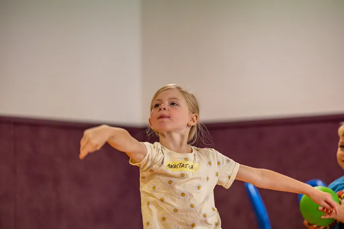 Ein kleines Mädchen mit dem Namensschild „Anastasia“ streckt die Arme aus und blickt nach oben.