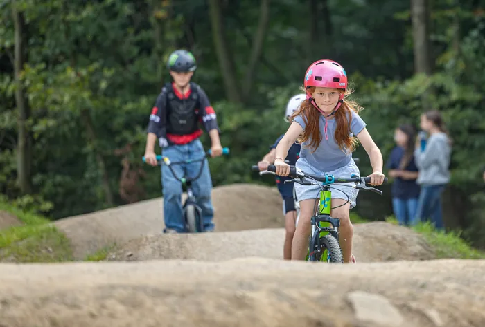 Ein Mädchen mit rosa Helm fährt auf einem Mountainbike über eine Dirt-Strecke im Bikepark Halver.