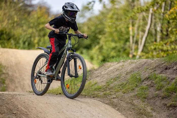 Ein Mountainbiker mit Helm und Schutzbrille fährt auf einem Erdweg in einem Bikepark.