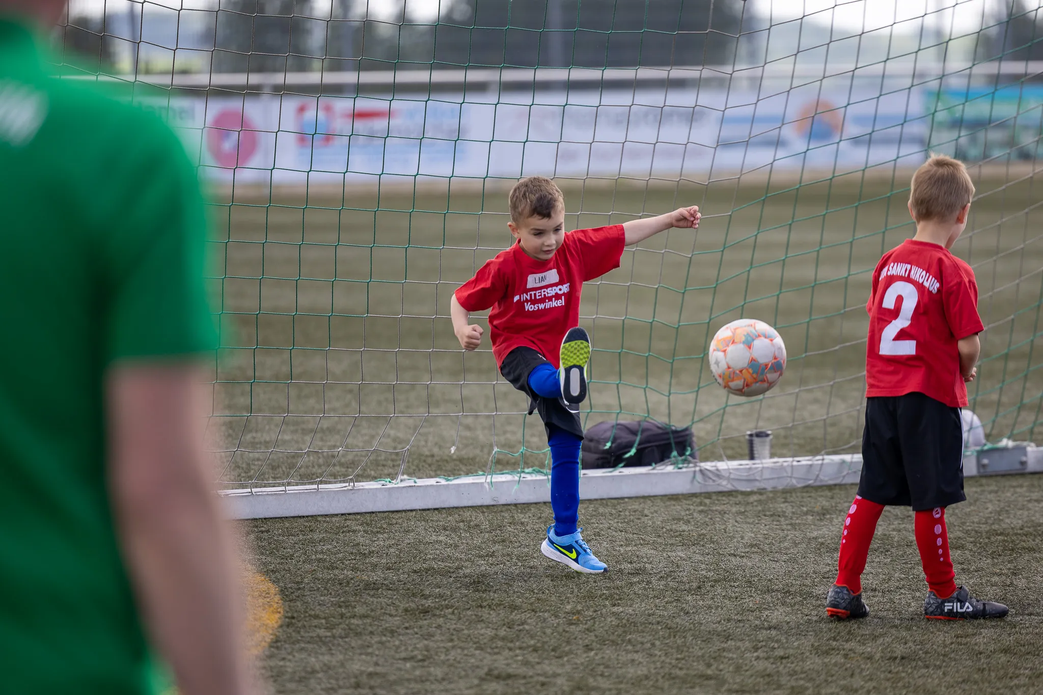 Zwei junge Fußballspieler treten vor einem Tor an, einer schießt auf den Ball, der andere versucht ihn zu blocken.