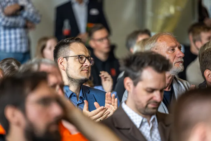 Ein Mann mit Brille und blauem Hemd klatscht bei der Jubiläumsfeier der Firma Janßen&Janßen.