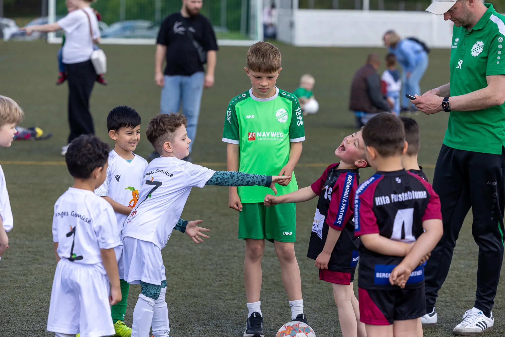 Junge Fußballspieler umringen einen Schiedsrichter während eines Turniers. Zwei Spieler reichen sich die Hände, während ein dritter weint.