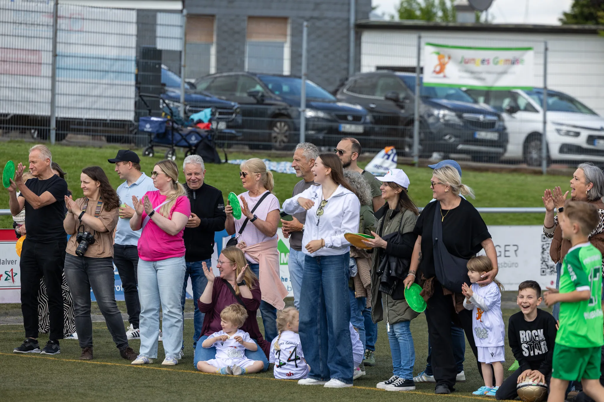 Zuschauer stehen am Spielfeldrand und applaudieren bei einem Fußballturnier für Kinder.